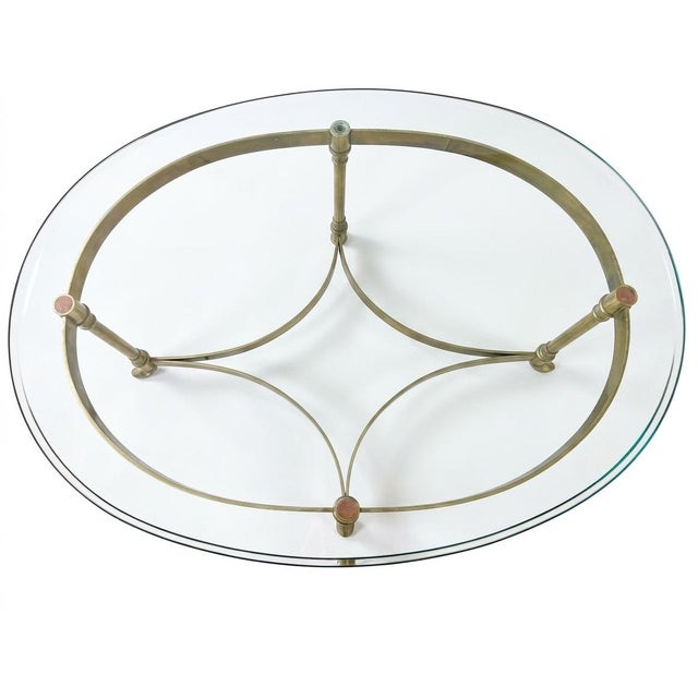 A chic Maison Jansen style coffee MJ table featuring an oval glass top on an elegant brass base with neoclassical...