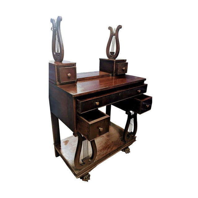 This is an antique writing desk with a vanity-style top. The desk features lyre-shaped legs and 5 drawers. The style is...