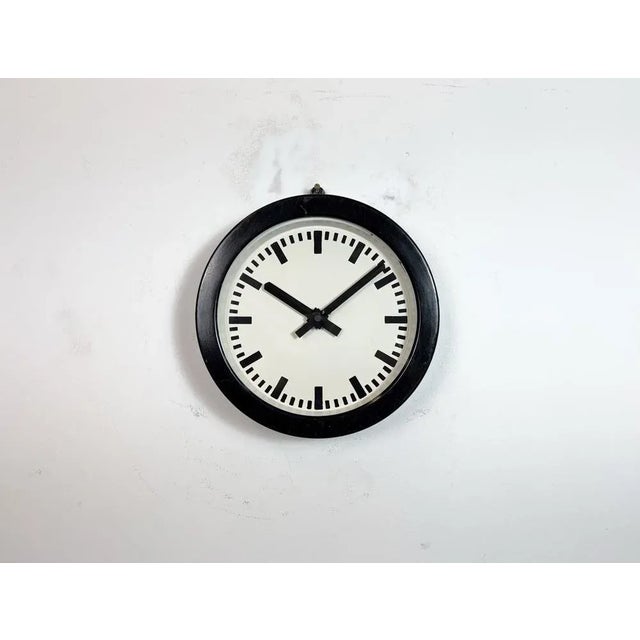 This wall clock was made in Germany during the 1950s. It features a black metal frame, a metal dial and a clear glass...