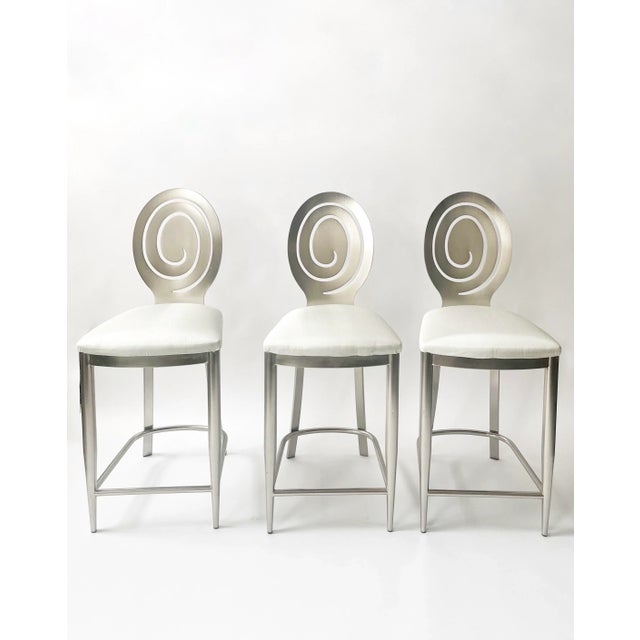 Set of three brushed nickel over steel spiral backed bar stools, newly upholstered in a silvery satin crepe fabric. Great...