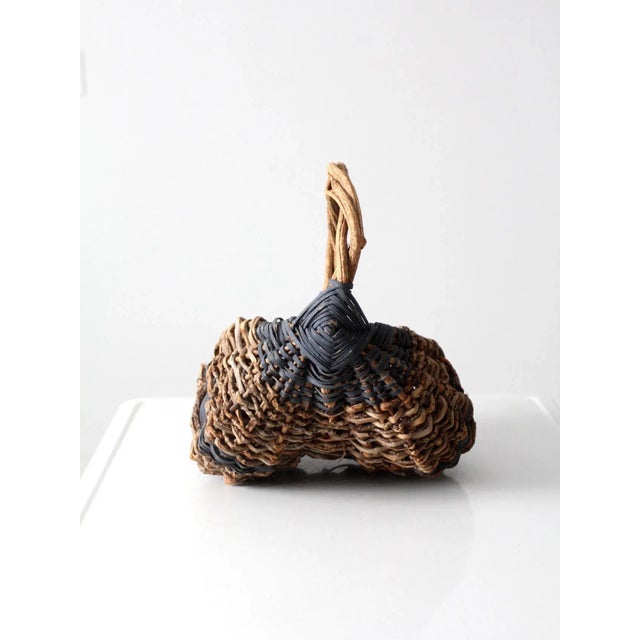 This antique primitive harvest basket features a traditional buttocks-style form with a rustic, twig-woven construction....