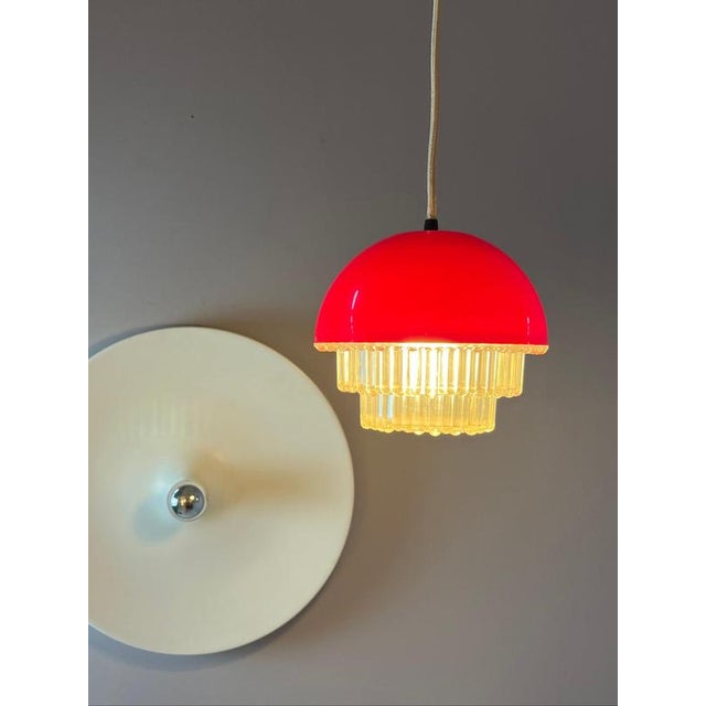 This red plastic pendant lamp in a space-age style impresses with its striking red dome and futuristic design. The...