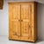 Two-door rustic armoire made of fir wood, featuring iron hardware and four panelled door sections. The piece is topped...