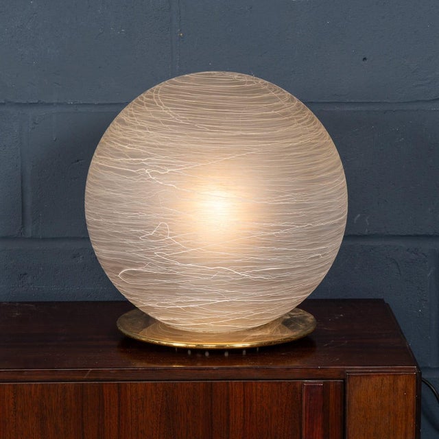 An elegant spherical frosted glass table lamp, crafted in Italy circa 1980. The globe features soft white striations that...