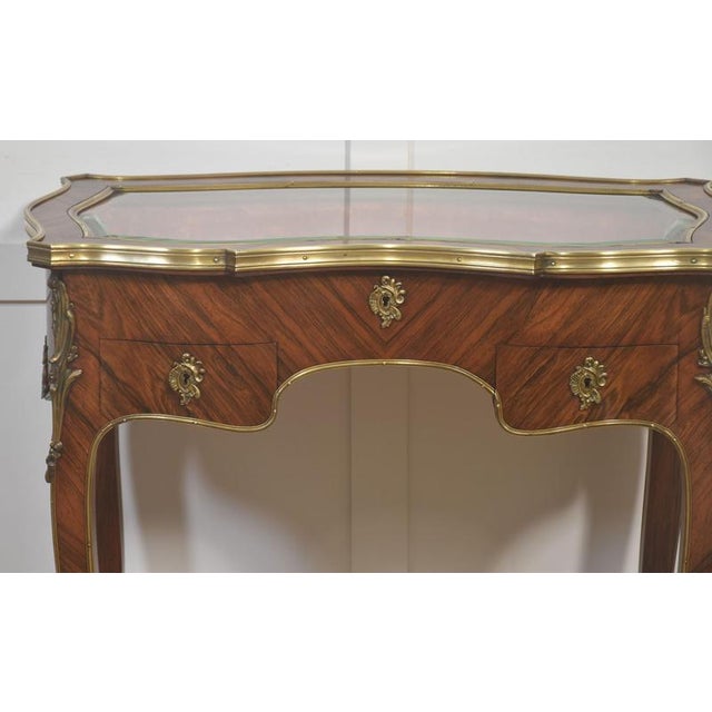 A refined French vitrine table of serpentine form, veneered in richly figured kingwood arranged in chevron and cross-...