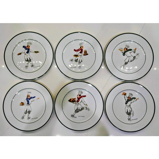 A whimsical vintage set of six “Skating Chefs” porcelain dessert plates designed by renowned culinary artist Guy Buffet....