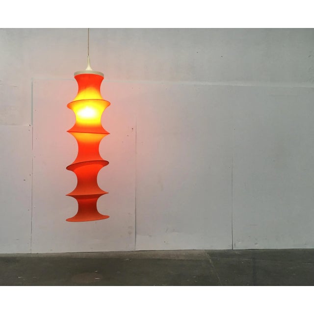 Mid Century Tube pendant lamp in orange by the luminaire manufacturer Aro. an orange stretch fabric that is stretched over...