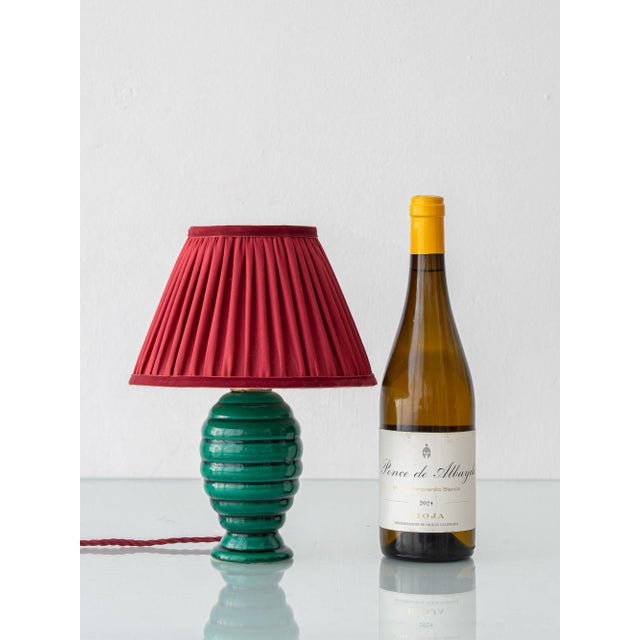 A small, jewel-toned French Art Deco table lamp from the 1930s, its emerald base paired with a new garnet silk pleated...