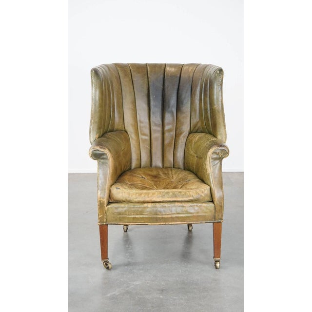 Offered is this large and well-worn green antique leather barrel back ear chair with beautiful colors and on casters....