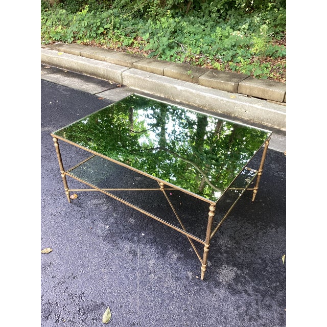A refined coffee table by featuring an elegant antiqued brass-finished metal frame paired with a mirrored glass top and...