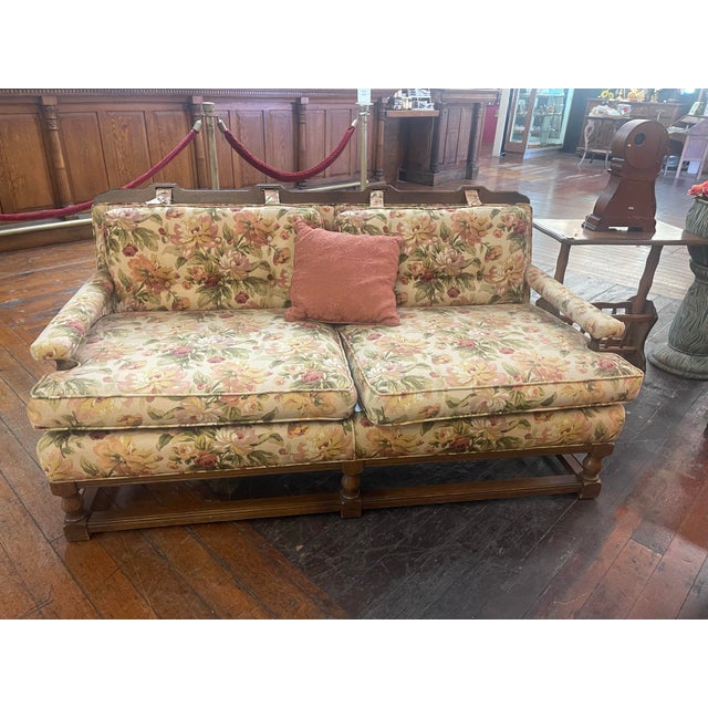 Charming vintage sofa featuring a classic English-inspired silhouette with carved wood detailing and a warm floral...