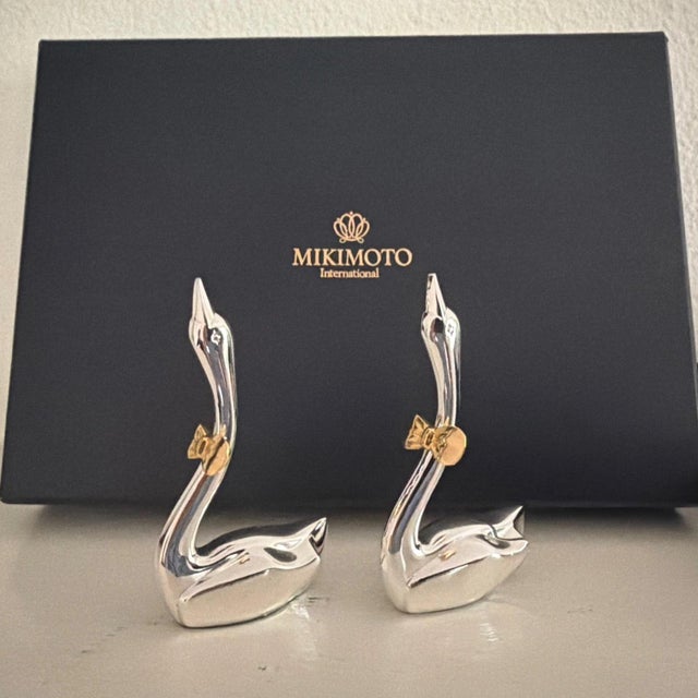 This product is a pair of Mikimoto silver-plated swans with gold bows, designed as wedding place cards. Adds touch of...