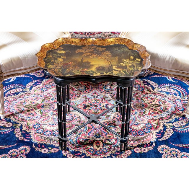 A lacquered tray table decorated with a hand-painted landscape featuring trees, birds, water and a distant tower, an...