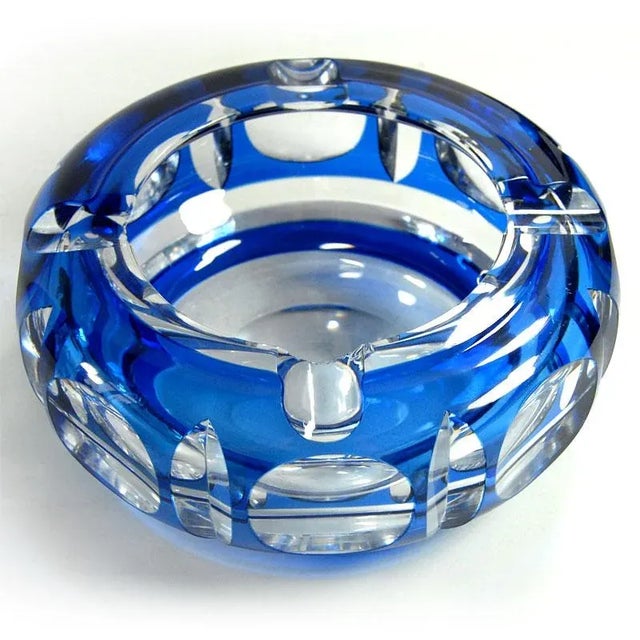 A large, solid ashtray made of cut crystal glass in a sapphire garnet color. It comes from the Belgian manufacturer Val St...