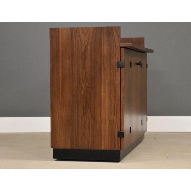 A mid century modern walnut rolling bar with black accents and a black formica top designed by Milo Baughman for...