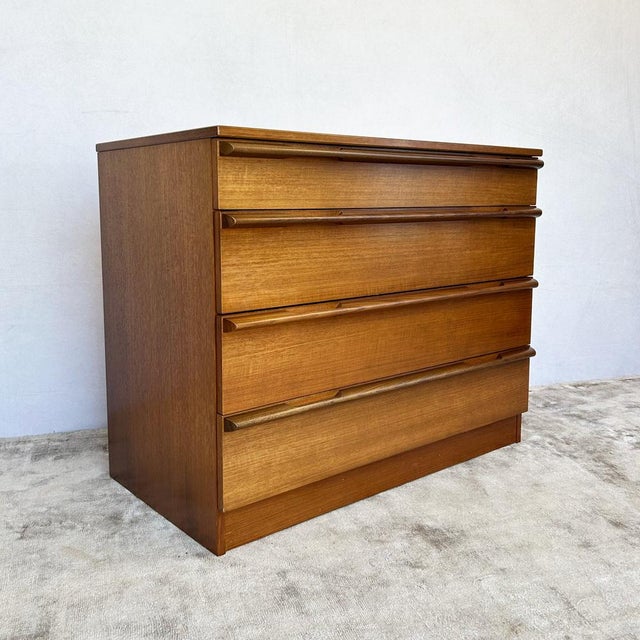 Teak-veneered carcase construction raised on a plinth base. Four full-width graduated drawers with sculptural solid...