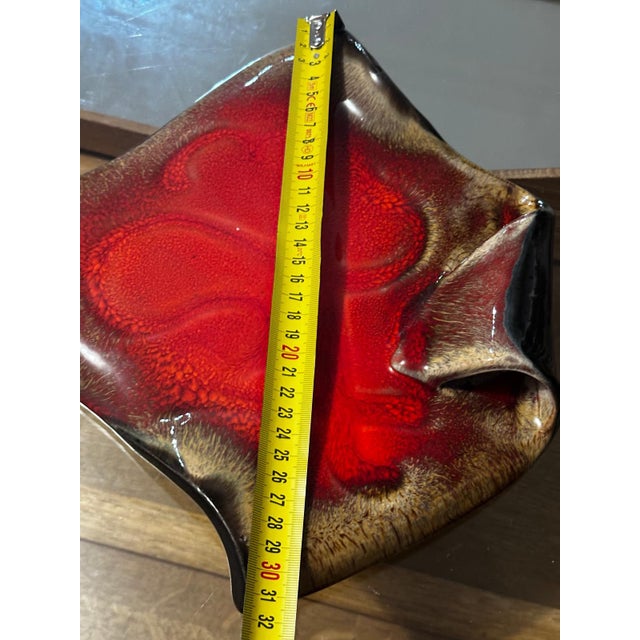 A free-form ceramic trinket dish or bowl, covered in a striking, vibrant red glaze with brown and black undertones....