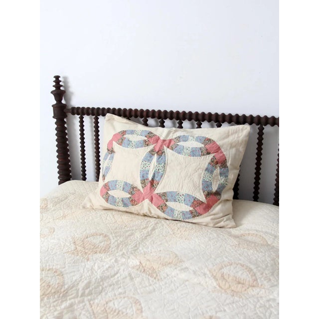 A vintage quilted pillow cover featuring a classic wedding ring pattern in soft floral pinks and blues against a warm...