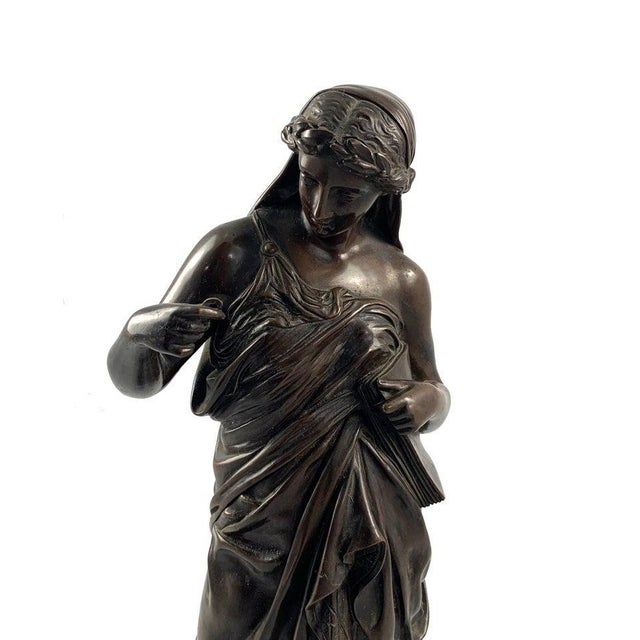 A french cast bronze figure of a classical maiden, circa 1900. Dark brown patination. Shown standing wearing draped robes....
