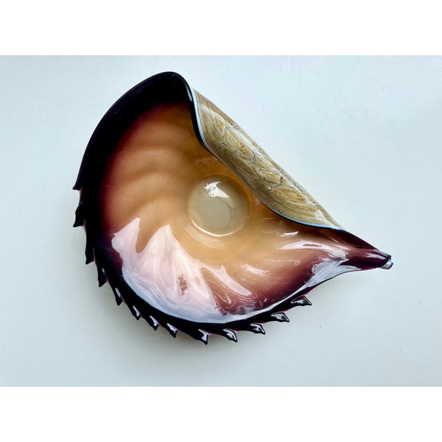 This handcrafted glass art vase in the shape of a conch shell comes from the renowned Polish glassworks Jozefina Art...