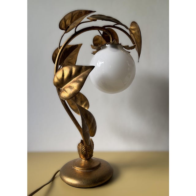 1970s table lamp designed in the Hollywood Regency / Florentine style. The structure features a curved, organic stem made...
