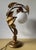 1970s table lamp designed in the Hollywood Regency / Florentine style. The structure features a curved, organic stem made...