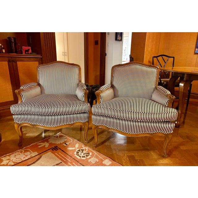 Late 20th-century armchairs, or bergères, upholstered in handsome white-and-brown striped silk-satin. Their seat cushions...