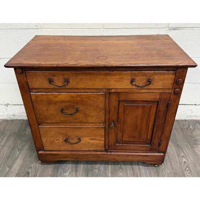 This is a gorgeous antique early-1900s Arts & Crafts oak washstand featuring three dovetailed drawers, a paneled cabinet...