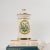 Charming 1970s ceramic apothecary jar featuring an elegant Sanicula botanical crest against creamy off-white ceramic...