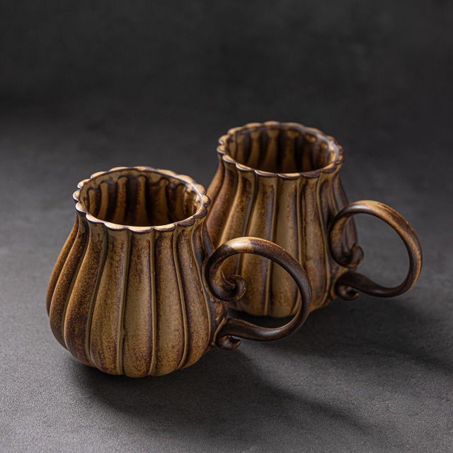 A pair of vintage-style ceramic mugs, designed in the shape of pumpkins with fluid, sculptural lines.