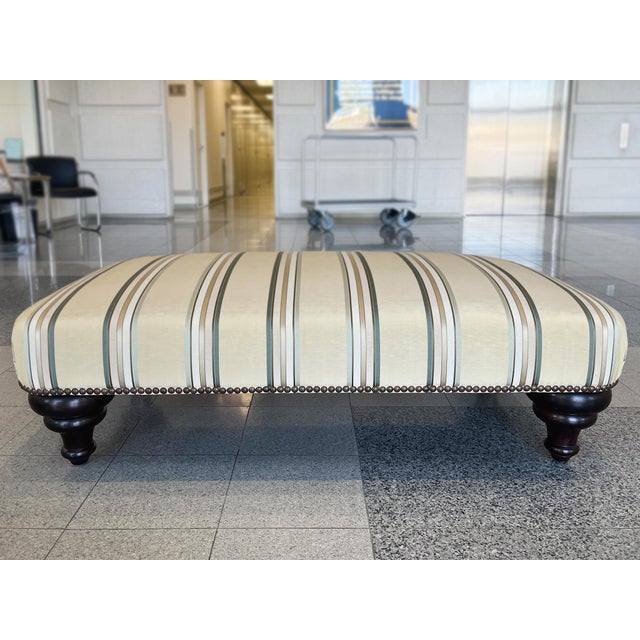 A vintage George Smith ottoman, hand-crafted with a pale yellow striped linen upholstery, brass studs, and turned mahogany...