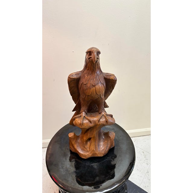 A beautiful hand carved wooden bald eagle with overlapping feathers and deeply grooved wings. The eagle is perched as its...