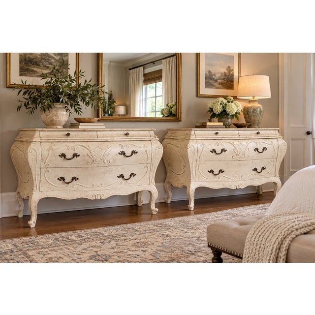 A striking matched pair of generously scaled French Provincial bombé commodes, each measuring an impressive 51 inches...