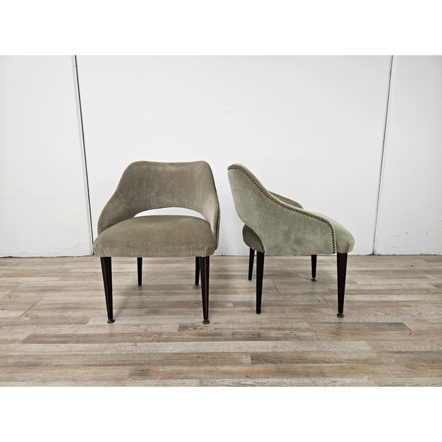 A pair of 1960s-era living room or bedroom armchairs, entirely upholstered in light green fabric and with wooden legs. The...