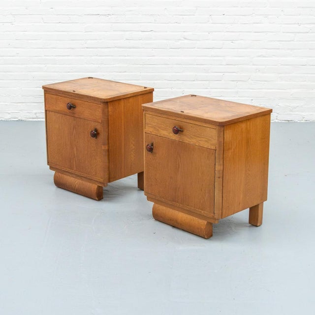 Set of two Art Deco bedside tables from the 1920s–30s, executed in wood with a warm honey-toned finish and a lively grain....