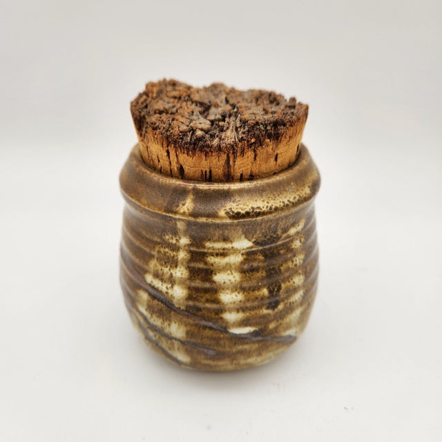 Small ribbed stoneware jar with variegated brown and cream glaze, fitted natural cork stopper, signed "LAIR" on base.
