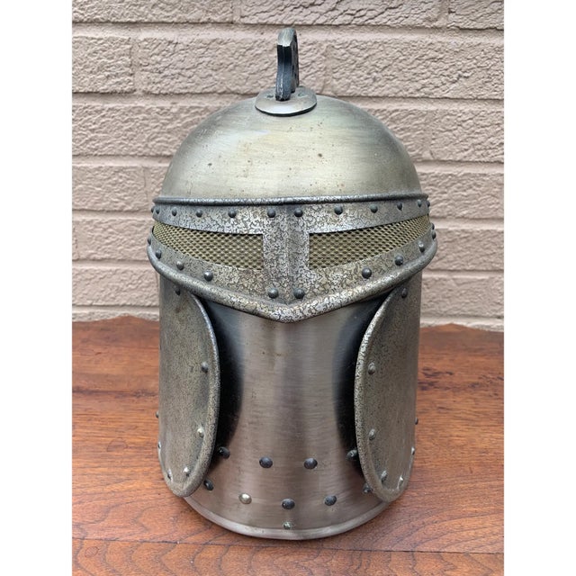 A vintage pewter ice bucket formed as a medieval knight’s helmet, detailed with riveted construction, a pierced visor, and...