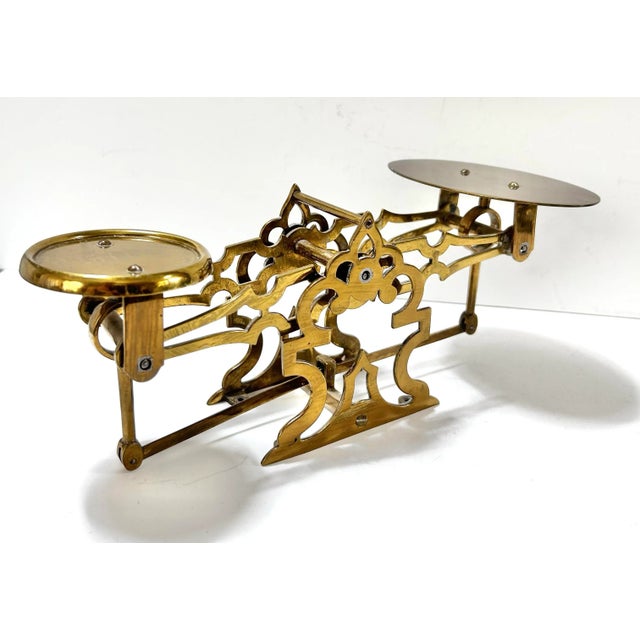 A decorative 1940s brass balance scale with unusually ornate pierced framework and two round weighing platforms. The...