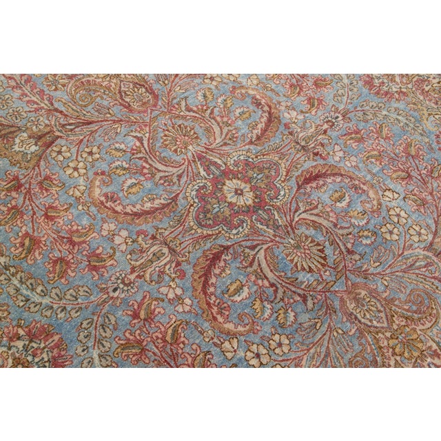 Beautiful antique Kirman hand-knotted wool rug with a blue color field. This Persian rug has beige and pink accents in a...