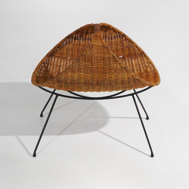 A 1950s woven rattan magazine rack with a metal frame, distinguished by its sculptural silhouette that combines the...