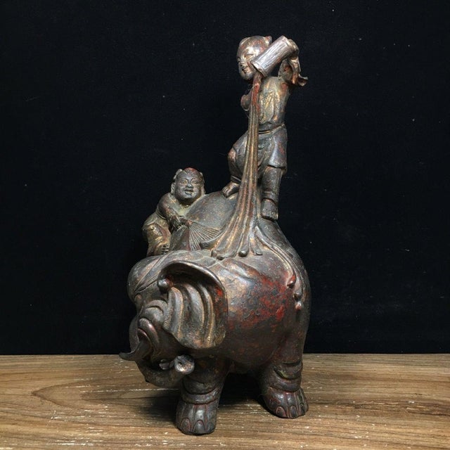 This charming vintage sculpture depicts a playful scene of two young boys interacting with a large elephant, a traditional...