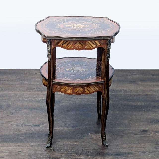 Antique two tier table using multiple woods with floral center medallion, surrounded by metal trim. The table rests on...
