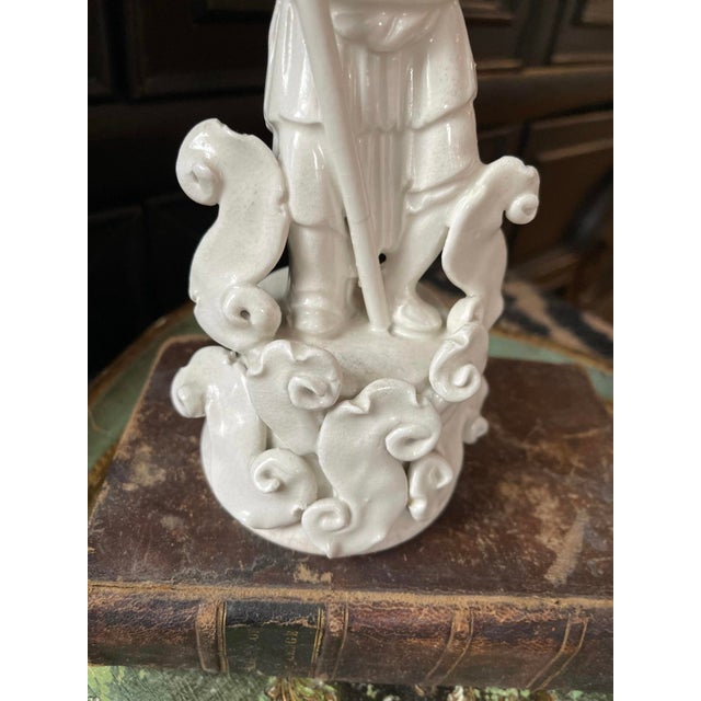 Early 20th century Blanc de Chine statue of a man standing atop a pedestal of waves, holding an uncapped decanter in a...