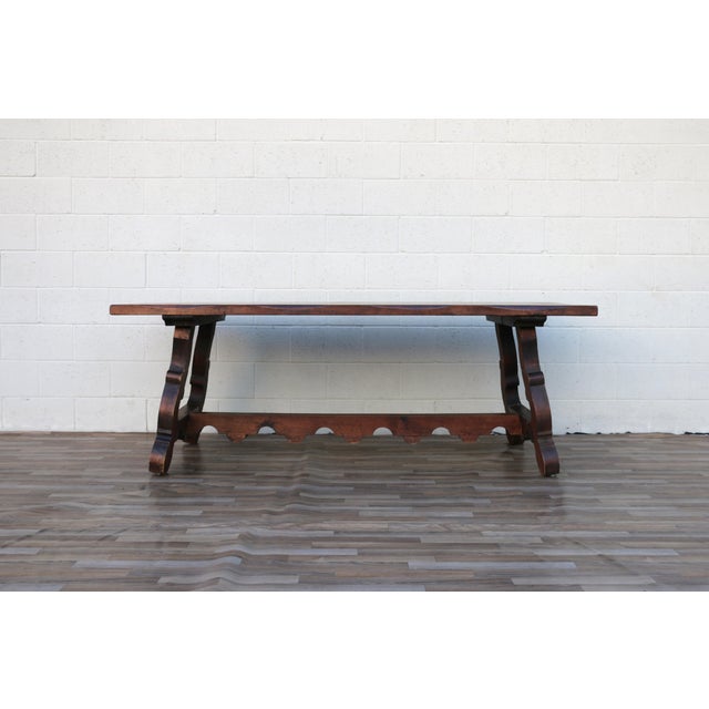 A striking Antique Spanish Revival trestle dining table crafted from solid wood, featuring a beautifully aged plank top...