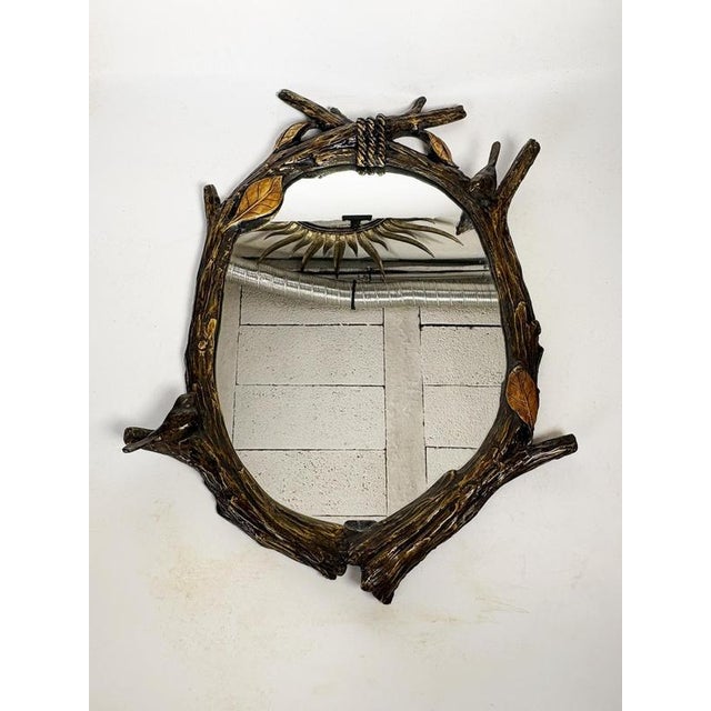 A decorative mirror adorned with a sculptural frame imitating intertwined tree branches, embellished with leaves and birds...