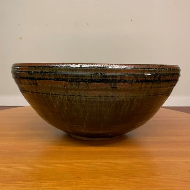 A dramatic large-scale studio pottery bowl, wheel-thrown in stoneware and richly glazed in earth tones, dating to the...