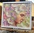 This oil on board painting features a serene female figure partially enveloped by a vibrant array of flowers, creating a...