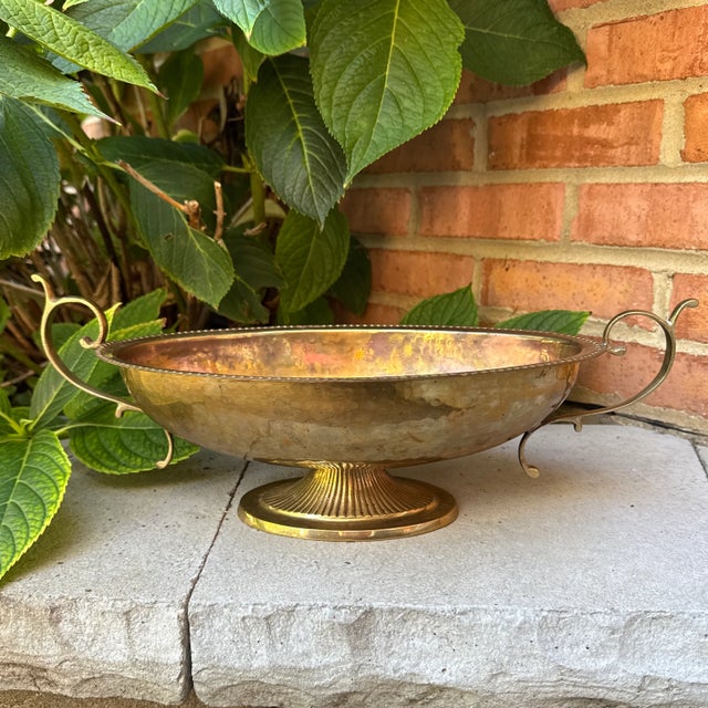 Vintage hammered brass pedestal bowl featuring elegant serpentine handles, rope edging, and a classic fluted pedestal. The...