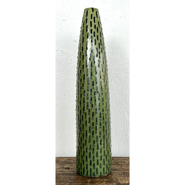 This vintage ceramic vase presents a tall, tapering conical form that narrows gracefully from a broad rounded base to a...