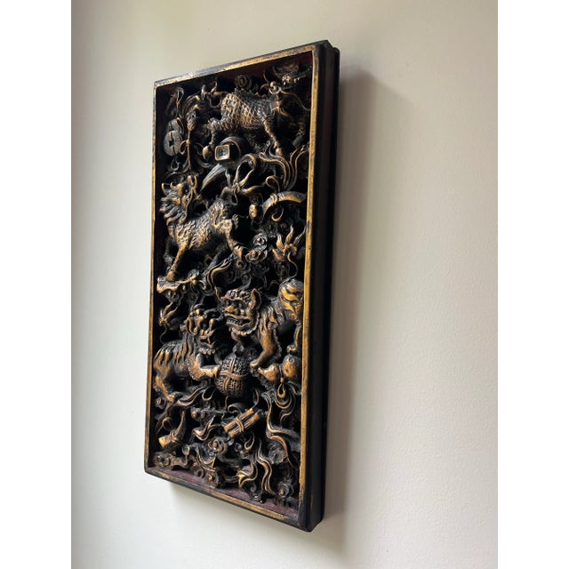 A dramatic and intricately carved wood panel in the Chinese decorative style, featuring expressive Foo dogs (guardian...